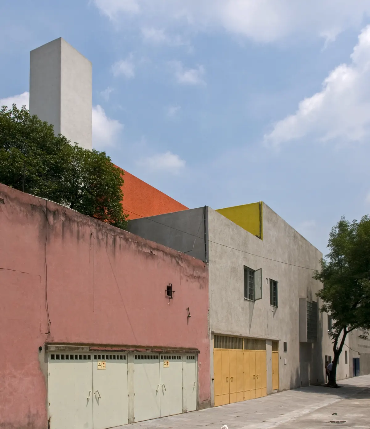 The street front of Casa Luis Barragán, with a pink wall, yellow and orange planes and the white water tower above